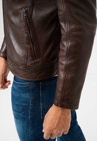 Bruine leren jas met een ritssluitingszak, getailleerd ontwerp en een soepele textuur, gecombineerd met blauwe denim jeans.