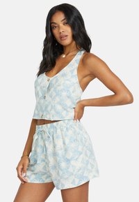 Ljusblå mönstrad croptop med knappar och matchande shorts med elastiskt midjeband som har geometriska mönster i vitt och blått.