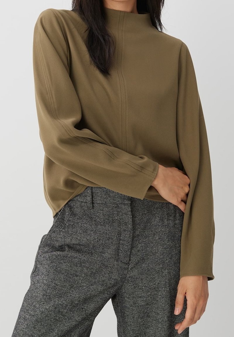 Haut à manches longues vert olive avec col montant, détails de couture subtils. Associé à un pantalon taille haute texturé gris.