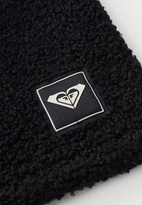 Gorro de forro polar negro con material texturizado. Muestra un parche cuadrado con un logo de corazón y detalles en blanco. Diseño suave y cálido.