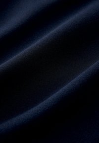 Marinblått tyg, slät yta med subtil lyster, har mjuka draperingar och veck. Ytan är jämn, utan synliga mönster eller utsmyckningar.
