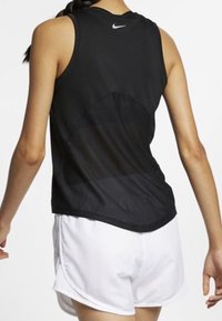 Svart sportlinne med genomskinlig bakpanel och rundad nederkant, med en liten vit Nike-logotyp vid halsringningen. Kombinerat med vita shorts.