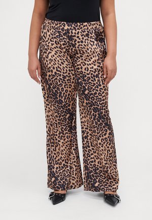 Pantalons larges à imprimé léopard en beige et noir. Tissu doux et fluide avec une taille élastique. Associés à des chaussures noires à bout pointu.