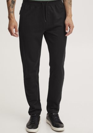 Black jogger pants made of soft fabric, featuring an elastic waistband with drawstring, side zip pockets, and tapered legs.
