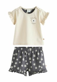 Top corto de manga corta color beige claro con bordes acampanados y bordado de flores, combinado con pantalones cortos gris oscuro con un patrón de margaritas blancas y dobladillo con volantes.