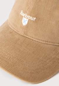 Καφέ καπέλο μπέιζμπολ από κορδόνι με λευκό και μπλε κεντημένο λογότυπο "Barbour" πάνω από το γείσο σε λευκό φόντο.