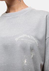 Jasnoszara bluza z bawełny z okrągłym dekoltem, z białym nadrukowanym tekstem i efektem rozprysku z przodu.