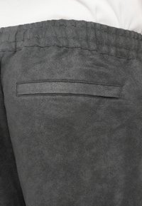 Calças cinzentas em suede sintético com um cós elástico, textura suave e um único bolso traseiro com abertura horizontal.