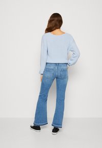Lyseblå strikkegenser med lange ermer, kombinert med utsvungne blå jeans og svarte joggesko. Genseren har rund hals og ribbestrikket tekstur.