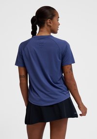 Niebieska sportowa koszulka z krótkim rękawem, okrągłym dekoltem, gładką teksturą i subtelnymi pionowymi akcentami na plecach. Połączona z czarną spódnicą.