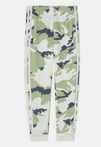 Pantalones de chándal Adidas con un patrón de camuflaje en verde, blanco y negro, cinturilla elástica y tres franjas blancas en los laterales.