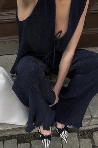 Tumed pleeditud jumpsuit sügava dekolteega ja nööri detailiga, koos terava otsaga zebra triibuliste kõrgete kontsadega, millel on must pael. Hõbedane kott kõrval.