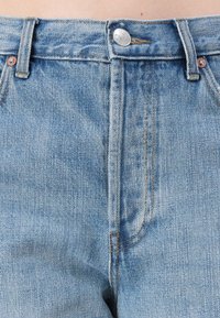 Zbliżenie jasnoniebieskich dżinsów z denimu pokazujące guzik, zamek błyskawiczny, szlufki na pasek, przeszycia i przednie kieszenie.