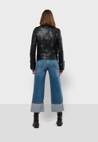 Crna kožna jakna s uzorkom zvijezda, uparena s širokim plavim trapericama koje imaju kontrastne traper rukave. Uklopljena s crnim masivnim čizmama.