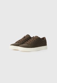 Zapatillas tejido marrón con un upper texturizado y suela de goma blanca. Presenta cordones redondos y un cuello acolchado para mayor comodidad.