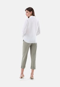 White long-sleeved shirt with a pointed collar, paired with light green cropped trousers, featuring rolled cuffs and a smooth texture.