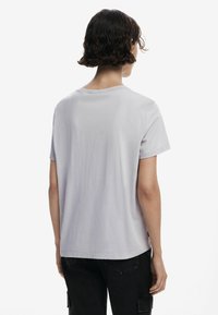T-shirt gris clair à manches courtes avec un col rond, une coupe décontractée et une texture en coton lisse, vu de l'arrière.