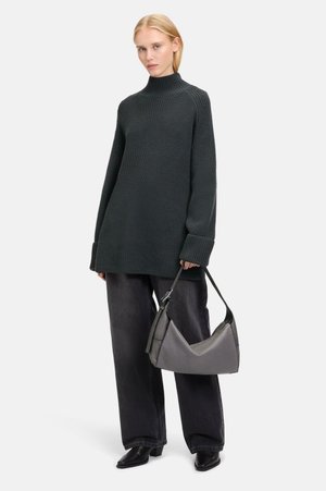 Maglione a maglia di colore verde scuro, oversize, con colletto alto, abbinato a jeans neri larghi e una borsa grigia curvata. Presenta maniche lunghe e un motivo strutturato.
