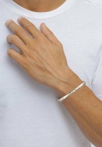 Silverarmband som bärs på ett handled, med en strukturerad, hamrad design. Enkel rund form med en slät metallfinish.