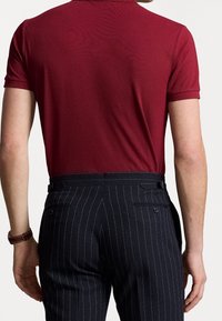 Bordowa koszulka polo połączona z granatowymi spodniami w paski. Koszulka ma klasyczny kołnierzyk; spodnie mają boczne i tylne kieszenie.