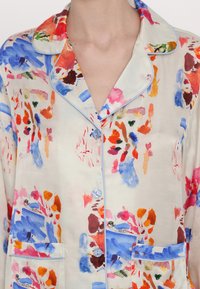 Cămașă de pijama din mătase cu model, prezentând desene florale albastre și roz, cu o margine albastră deschisă și două buzunare frontale cu nasturi. Textură moale.