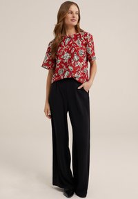 Blusa rossa a fiori con maniche corte, caratterizzata da un motivo floreale bianco e nero. Abbinata a pantaloni neri a gamba larga.