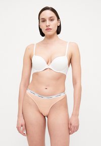 Bela push-up modrčka in nude tangice z elastičnim pasom s Calvin Klein logotipom. Gladko blago, nastavljive naramnice in zasnova z minimalno pokritostjo.