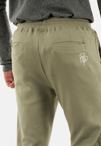 Khaki bukser med tekstureret overflade, elastisk talje, to baglommer og en hvid logo-detalje på bagsiden.