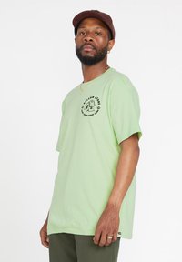 Camiseta de algodón verde claro con mangas cortas, con un estampado gráfico en negro en el frente y un corte relajado.