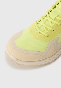 Ljusgrön sneaker med nätmaterial och släta beige detaljer. Har rundad tå, strukturerad yta och snörningsdesign.