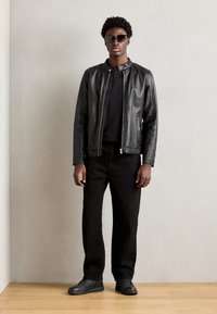 Chaqueta de cuero negra con un acabado suave, camiseta negra, pantalones negros y zapatos negros. Gafas de sol y un diseño minimalista.