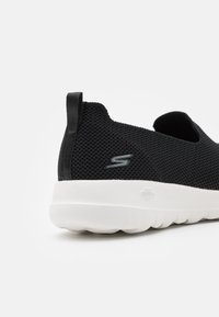 Schwarzer Netz-Schlüpfschuh mit strukturiertem Obermaterial, weißer Gummisohle und einer Zuglasche hinten. Mit einem Logo an der Seite.