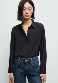 Svart långärmad skjorta med krage, med knappstängning och slät textur, kombinerad med högmidjade mörkblå jeans.