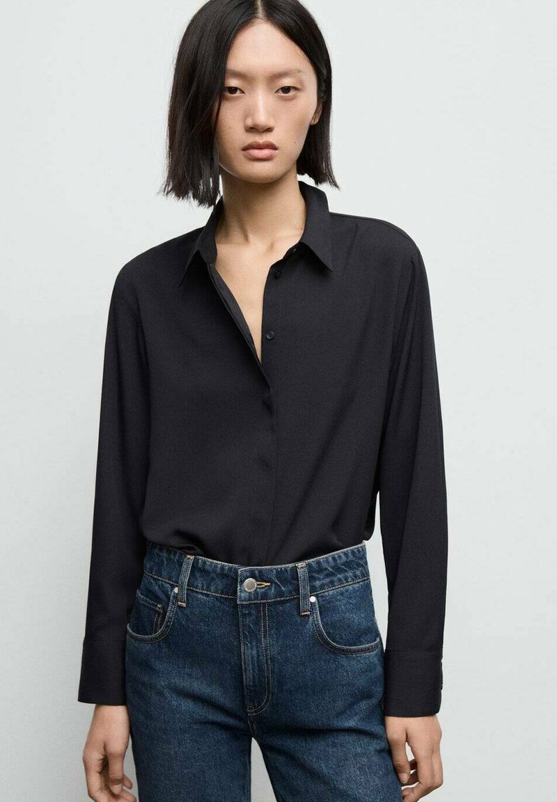 Svart långärmad skjorta med krage, med knappstängning och slät textur, kombinerad med högmidjade mörkblå jeans.