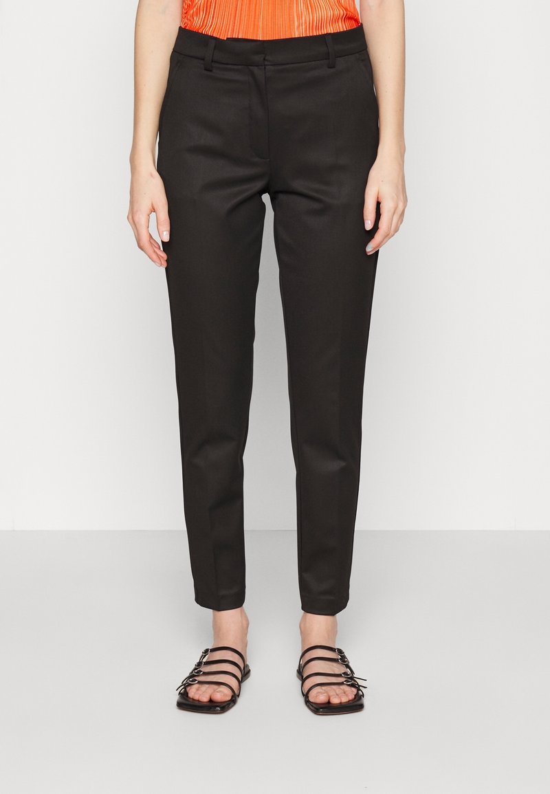 Czarne, dopasowane spodnie o gładkim wykończeniu, o wąskim kroju i bocznych kieszeniach, zestawione z czarnymi sandałami na paski i pomarańczową bluzką.