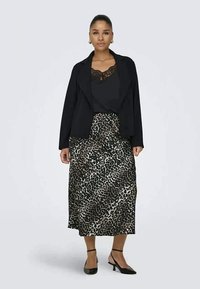 Blazer preto sobre uma blusa preta com detalhes em renda, combinado com uma saia de cetim com padrão de leopardo. Sapatos de salto pretos com tiras no tornozelo completam o look.