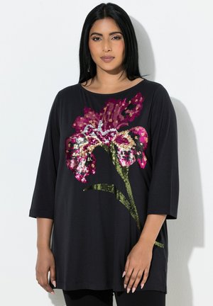 Svart oversize-topp med blommigt paljettdesign i rosa, vitt och guld. Tröjan har trekvartsärmar och rund halsringning.