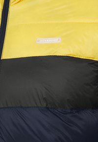 Yellow and black padded jacket featuring a smooth texture, a stitched design, and a subtle logo label on the chest.