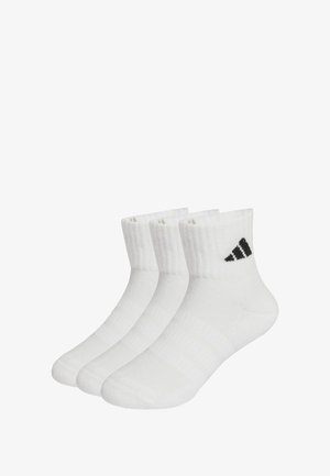Calcetines blancos hasta el tobillo en un paquete de tres. Textura de punto, puños acanalados, talones reforzados y logo de adidas en negro en el lado exterior.