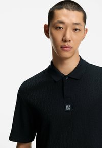 Polo nero con design texture, maniche corte e colletto classico. Presenta un piccolo logo "HUGO" sul petto.