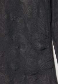 Svart stickat tyg med en texturerad design, som har subtila upphöjda prickar och en genomskinlig karaktär. Slät och något sträcker sig tyg.