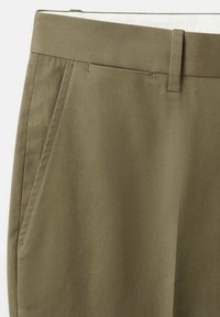 Nahaufnahme der Taille khakifarbener Hosen mit Gürtelschlaufen und Seitentaschen-Details vor einem einfarbigen Hintergrund.