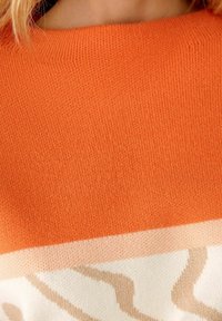 Maglione lavorato a maglia di un vivace colore arancione con una consistenza liscia, e una sezione crema che presenta un motivo beige ondulato nella parte inferiore.