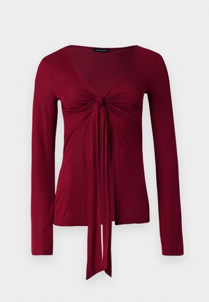 Bordo krāsas garroku tops ar V-veida izgriezumu un priekšpusē mezglotu detaļu ar pagarinātām auduma lentēm, kas karājas uz leju.