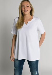 T-shirt bianco con scollo a V e maniche corte, realizzato in un tessuto liscio, vestibilità ampia, indossato con jeans blu strappati, dotati di tasche.
