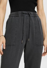 Dunkelgraue, elastische Hose mit Gummibund verfügt über einen Kordelzug, Seitentaschen und einen strukturierten Stoff mit einem dezenten Glanz.