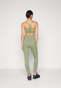 Olive green sports bra with a crisscross back design, paired with form-fitting leggings in the same color and black athletic shoes.