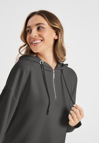Grijze hoodie met een ritskraag, verstelbare trekkoorden en een casual pasvorm. Gladde textuur en minimale branding aan de voorkant.