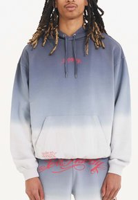 Sudadera con capucha en un degradado de azul-gris a blanco. Cuenta con un bolsillo frontal y texto gráfico en rojo. Fabricada con un tejido suave y texturizado.