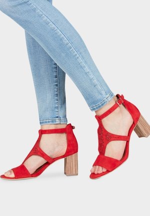 Røde ruskindssandaler med blokhæl, udskæringsdesign og ankelrem, kombineret med lyseblå skinny jeans.
